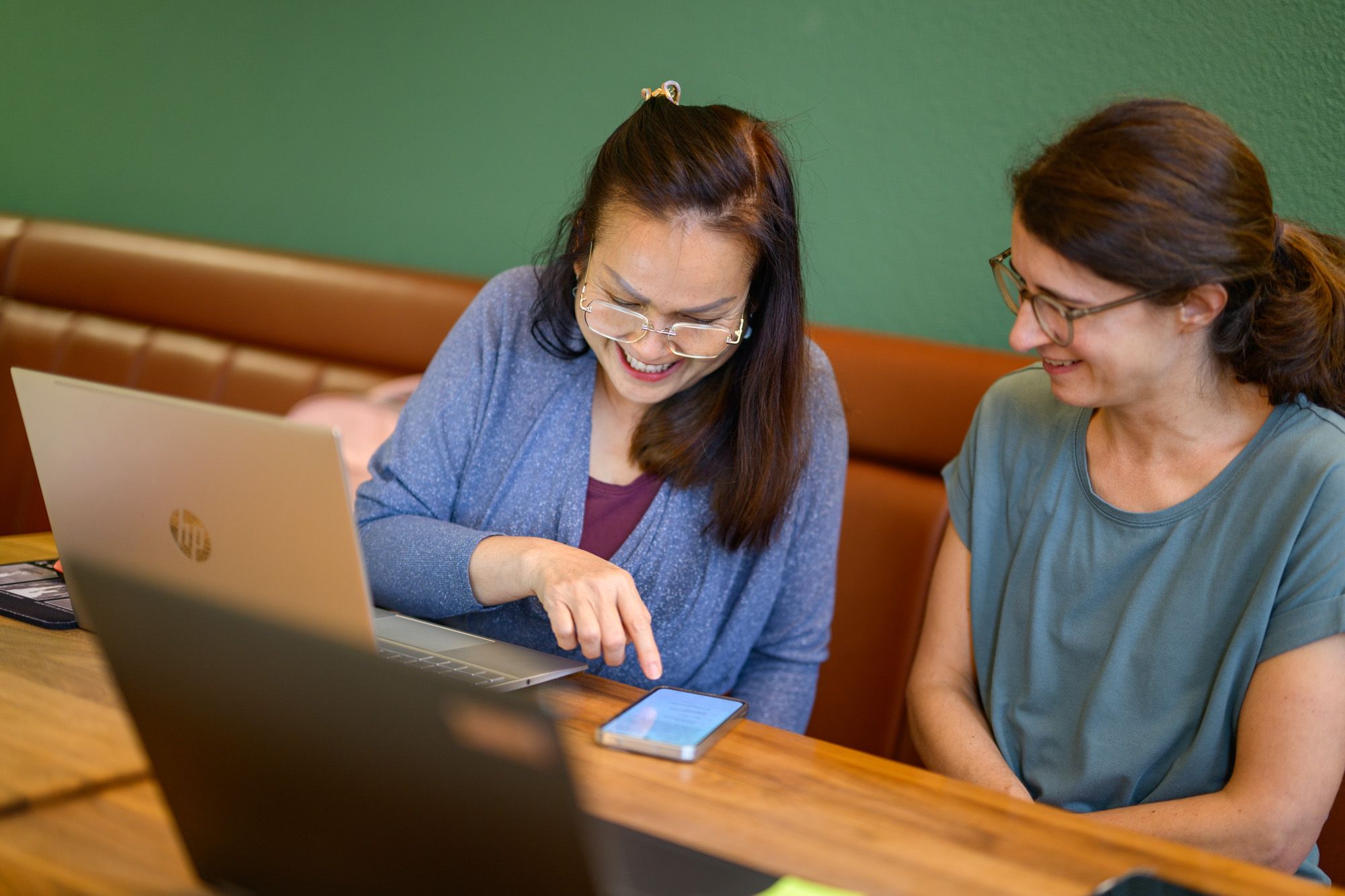 Die Lernstuben-Leitung erklärt einer Besucherin etwas am Handy. Die beiden sitzen gemütlich auf der Bank.